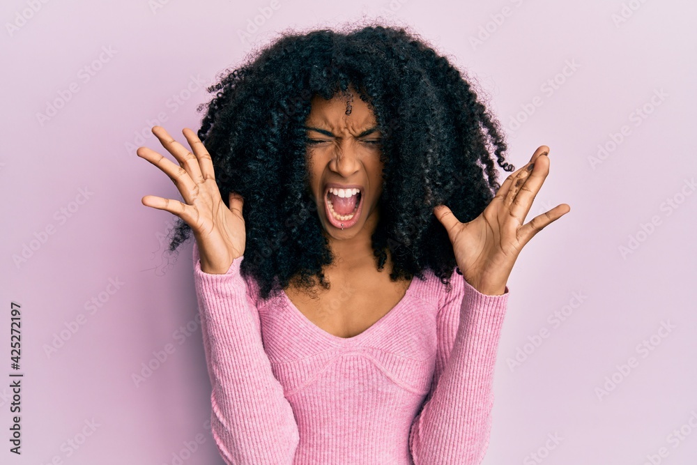 African american woman with afro hair wearing casual pink shirt celebrating mad and crazy for success with arms raised and closed eyes screaming excited. winner concept African american woman with afro hair wearing casual pink shirt celebrating mad and crazy for success with arms raised and closed eyes screaming excited. winner concept