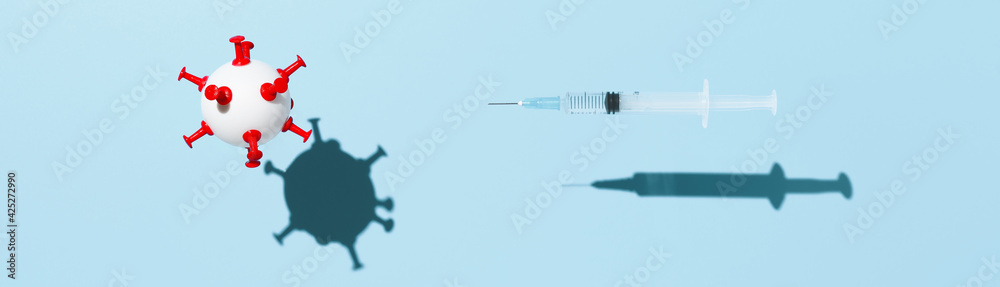 Coronavirus vaccination concept. A medical syringe with a vaccine against COVID-19, and a white ball in form virus, levitating over pastel blue background. Top view, wide banner Coronavirus vaccination concept. A medical syringe with a vaccine against COVID-19, and a white ball in form virus, levitating over pastel blue background. Top view, wide banner