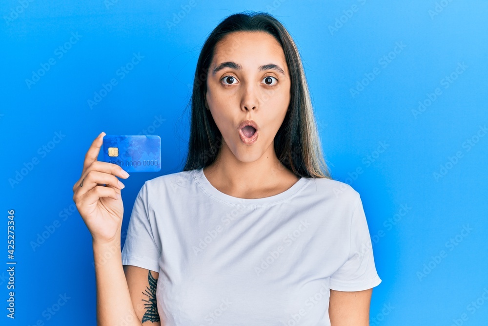 Young hispanic woman holding credit card scared and amazed with open mouth for surprise, disbelief face Young hispanic woman holding credit card scared and amazed with open mouth for surprise, disbelief face