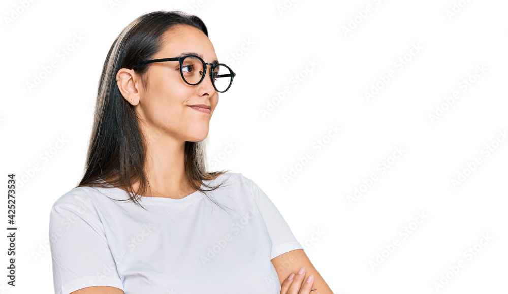 Young hispanic woman wearing casual white t shirt looking to the side with arms crossed convinced and confident Young hispanic woman wearing casual white t shirt looking to the side with arms crossed convinced and confident