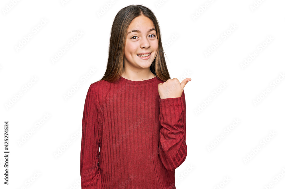 Beautiful brunette little girl wearing casual sweater smiling with happy face looking and pointing to the side with thumb up. Beautiful brunette little girl wearing casual sweater smiling with happy face looking and pointing to the side with thumb up.