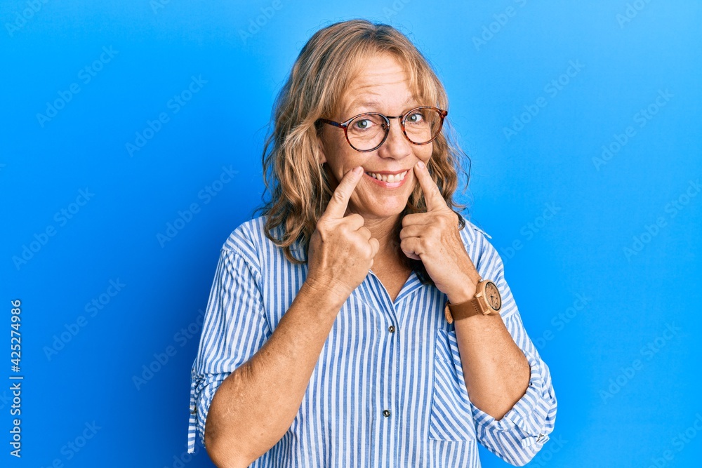 Middle age blonde woman wearing casual clothes and glasses smiling with open mouth, fingers pointing and forcing cheerful smile Middle age blonde woman wearing casual clothes and glasses smiling with open mouth, fingers pointing and forcing cheerful smile