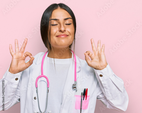 Beautiful hispanic woman wearing doctor uniform and stethoscope relax and smiling with eyes closed doing meditation gesture with fingers. yoga concept.