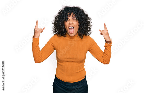Young hispanic woman wearing casual clothes shouting with crazy expression doing rock symbol with hands up. music star. heavy music concept.