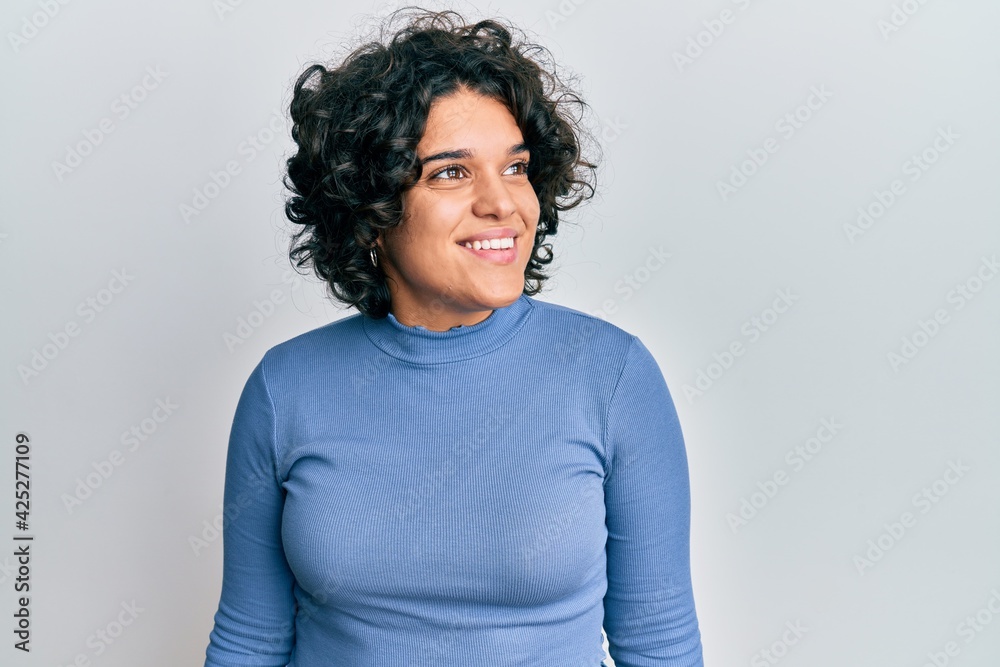 Fototapeta premium Young hispanic woman with curly hair wearing casual clothes looking to side, relax profile pose with natural face and confident smile.