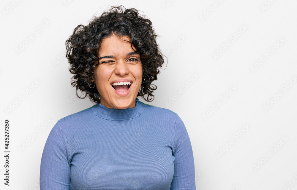 Young hispanic woman with curly hair wearing casual clothes winking looking at the camera with sexy expression, cheerful and happy face. Young hispanic woman with curly hair wearing casual clothes winking looking at the camera with sexy expression, cheerful and happy face.