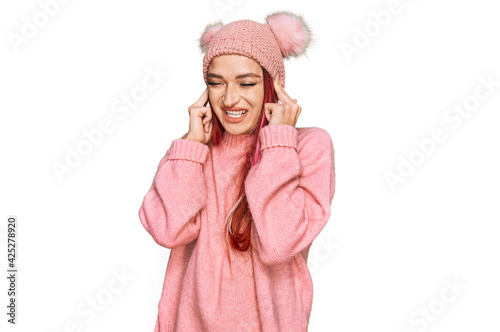 Young caucasian woman wearing casual clothes and wool cap covering ears with fingers with annoyed expression for the noise of loud music. deaf concept.