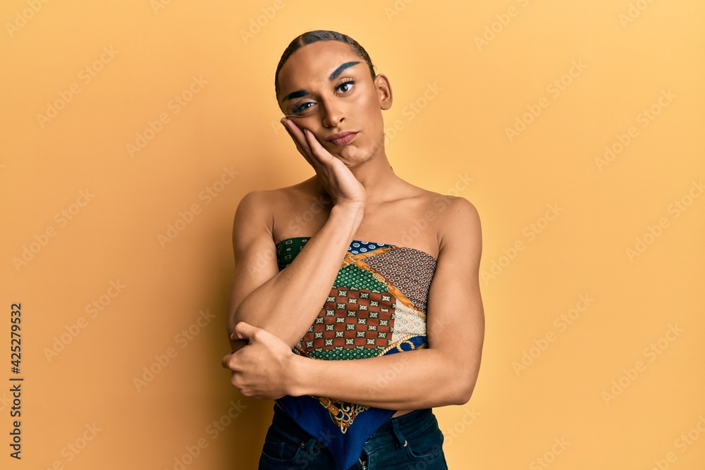 Hispanic man wearing make up and long hair wearing womans top thinking looking tired and bored with depression problems with crossed arms. Hispanic man wearing make up and long hair wearing womans top thinking looking tired and bored with depression problems with crossed arms.