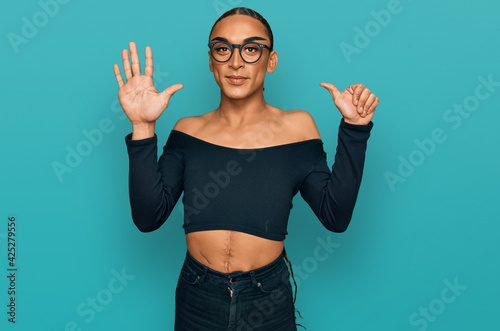 Hispanic transgender man wearing make up and long hair wearing women clothes showing and pointing up with fingers number six while smiling confident and happy.