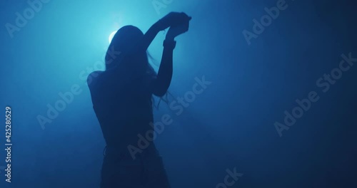 Dancing young girl in cloud of smoke, blue night club light. Modern dance, 4k video. Mysterious moving female silhouette