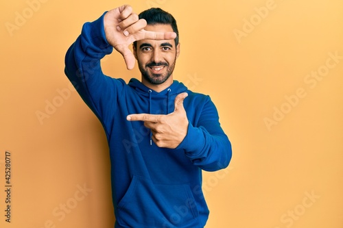 Young hispanic man wearing casual clothes smiling making frame with hands and fingers with happy face. creativity and photography concept. © Krakenimages.com