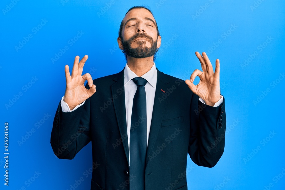 Attractive man with long hair and beard wearing business suit and tie relax and smiling with eyes closed doing meditation gesture with fingers. yoga concept. Attractive man with long hair and beard wearing business suit and tie relax and smiling with eyes closed doing meditation gesture with fingers. yoga concept.