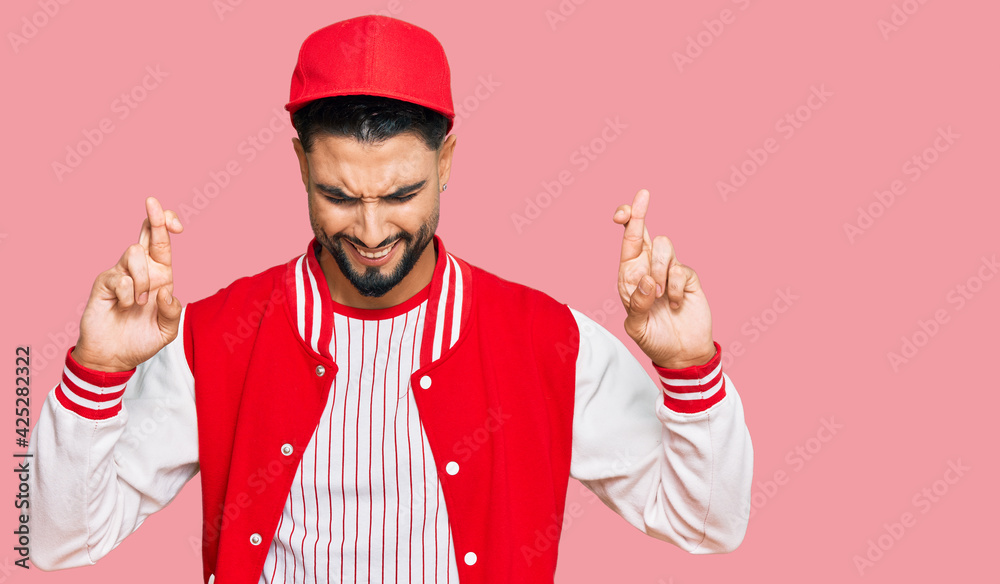 Young man with beard wearing baseball uniform gesturing finger crossed smiling with hope and eyes closed. luck and superstitious concept. Young man with beard wearing baseball uniform gesturing finger crossed smiling with hope and eyes closed. luck and superstitious concept.