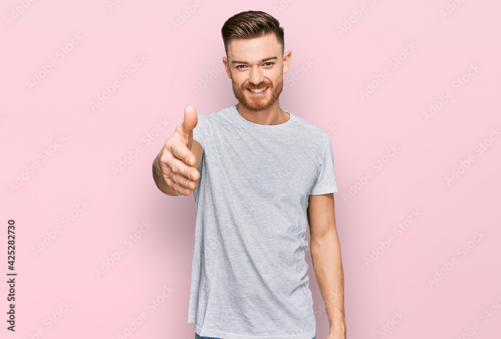 Young redhead man wearing casual grey t shirt smiling friendly offering handshake as greeting and welcoming. successful business. Young redhead man wearing casual grey t shirt smiling friendly offering handshake as greeting and welcoming. successful business.