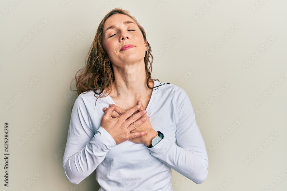 Young blonde woman wearing casual clothes smiling with hands on chest with closed eyes and grateful gesture on face. health concept. Young blonde woman wearing casual clothes smiling with hands on chest with closed eyes and grateful gesture on face. health concept.