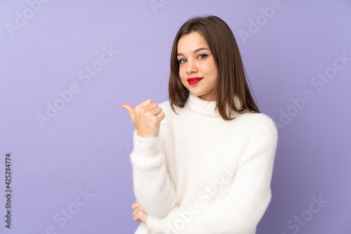 Teenager girl isolated on purple background pointing to the side to present a product
