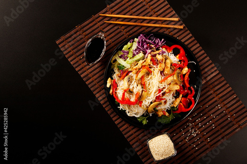 Japchae, Korean glass noodle stir fry. Korean glass japche noodles with stewed chicken with sesame vegetables and sauce on a black background.  Top view. Japchae Asian cuisine. Funchose