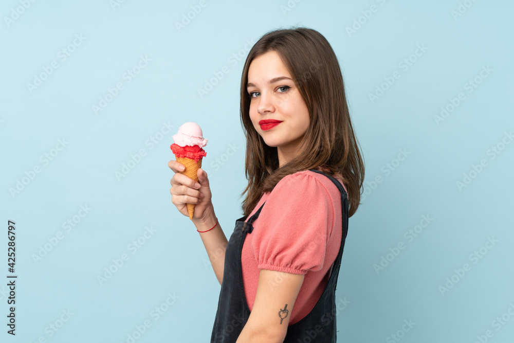 Teenager girl holding a cornet ice cream isolated on blue background smiling a lot Teenager girl holding a cornet ice cream isolated on blue background smiling a lot