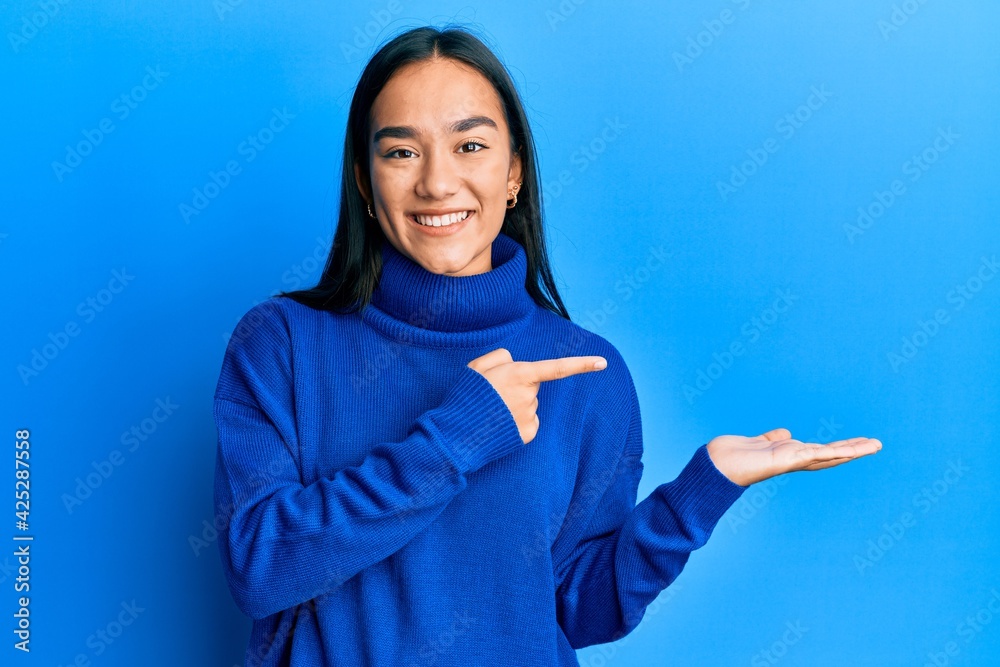 Young asian woman wearing casual winter sweater amazed and smiling to the camera while presenting with hand and pointing with finger.