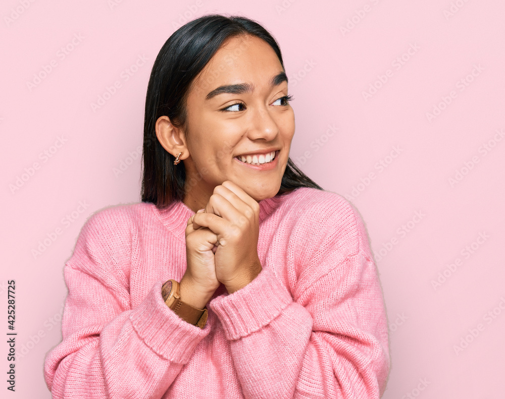 Young asian woman wearing casual winter sweater laughing nervous and excited with hands on chin looking to the side Young asian woman wearing casual winter sweater laughing nervous and excited with hands on chin looking to the side