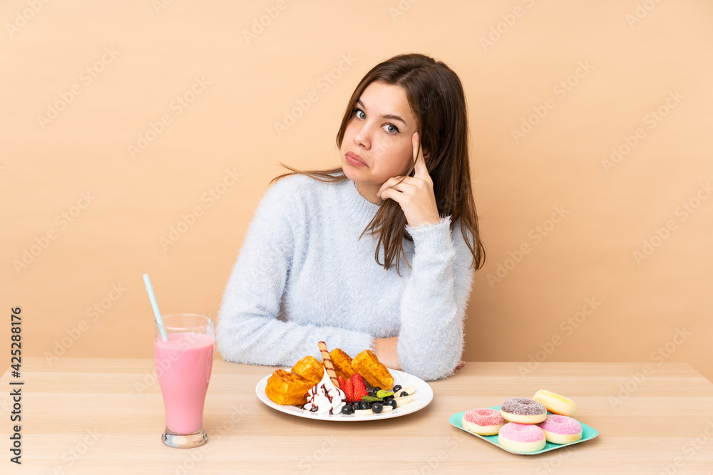 Teenager girl eating waffles isolated on beige background thinking an idea Teenager girl eating waffles isolated on beige background thinking an idea