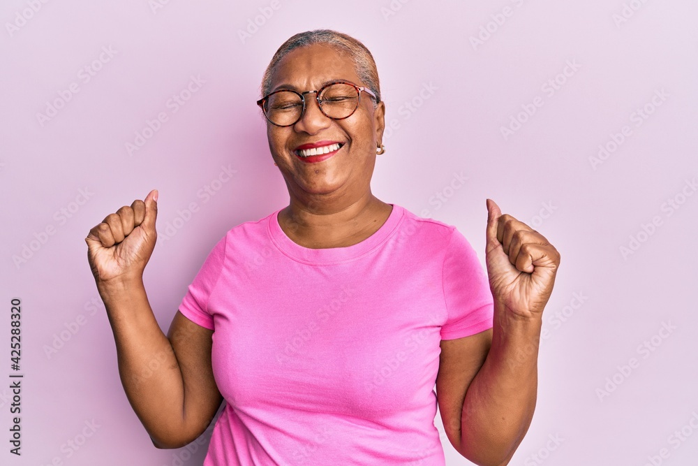 Senior african american woman wearing casual clothes and glasses very happy and excited doing winner gesture with arms raised, smiling and screaming for success. celebration concept. - obrazy, fototapety, plakaty 