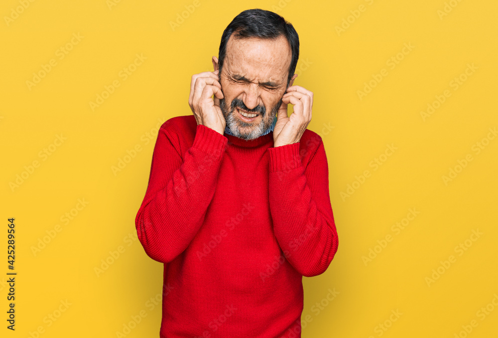 Middle age hispanic man wearing casual clothes covering ears with fingers with annoyed expression for the noise of loud music. deaf concept.