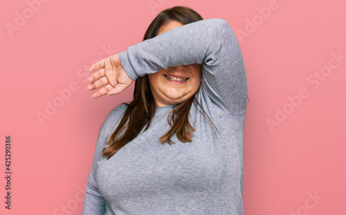 Beautiful brunette plus size woman wearing casual clothes covering eyes with arm smiling cheerful and funny. blind concept.