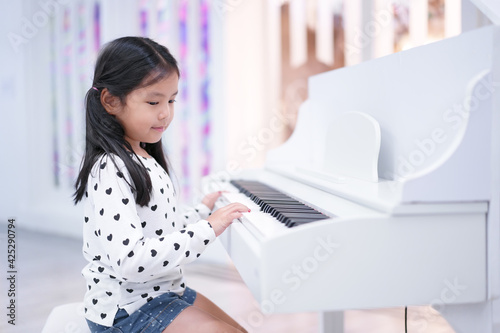 asian child cute or kid girl musician smile and happy playing white piano or electone to song show on stage or people learn at music school for artist education photo