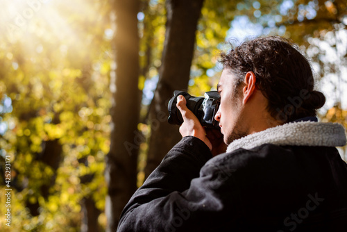 Young man taking pictures in the Autumn park. Photographer shooting fall landscapes