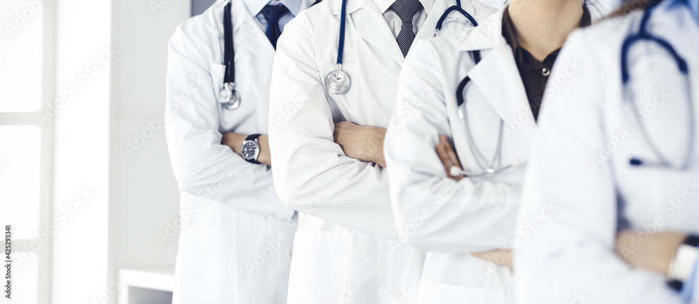 Group of modern doctors standing as a team with arms crossed in hospital office. Medical help, insurance in health care, best desease treatment and medicine concept Group of modern doctors standing as a team with arms crossed in hospital office. Medical help, insurance in health care, best desease treatment and medicine concept