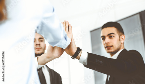 Business people group showing teamwork, joining hands and giving five to each other in modern office. Success concept