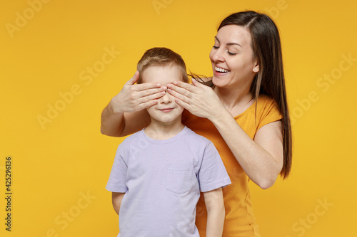 Happy young woman have fun with child baby boy 5-6-7 years old in violet tshirt Mommy little kid son close eyes with hands play guess who isolated on yellow background studio Mother's Day love family © ViDi Studio