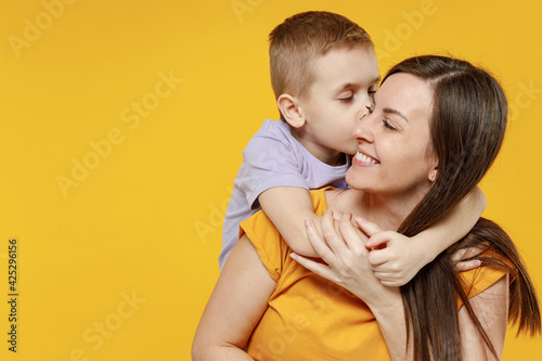 Happy young woman have fun with cute child baby boy 5-6-7 years old in violet t-shirt. Mommy little kid son posing together hugs isolated on yellow background studio. Mother's Day love family concept.