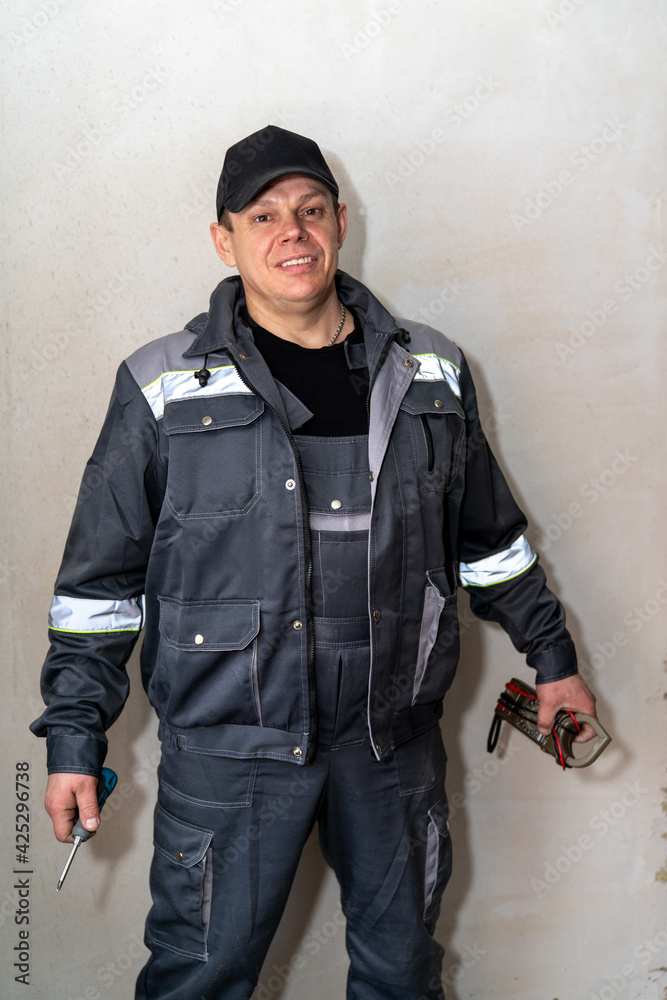 an electrician in overalls with a multimeter and a wrench in his hands an electrician in overalls with a multimeter and a wrench in his hands