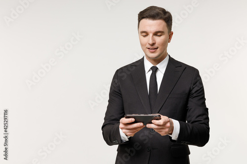 Young employee business corporate lawyer man wear classic formal black grey suit shirt tie work in office play racing on mobile phone hold gadget smartphone video games isolated on white background.
