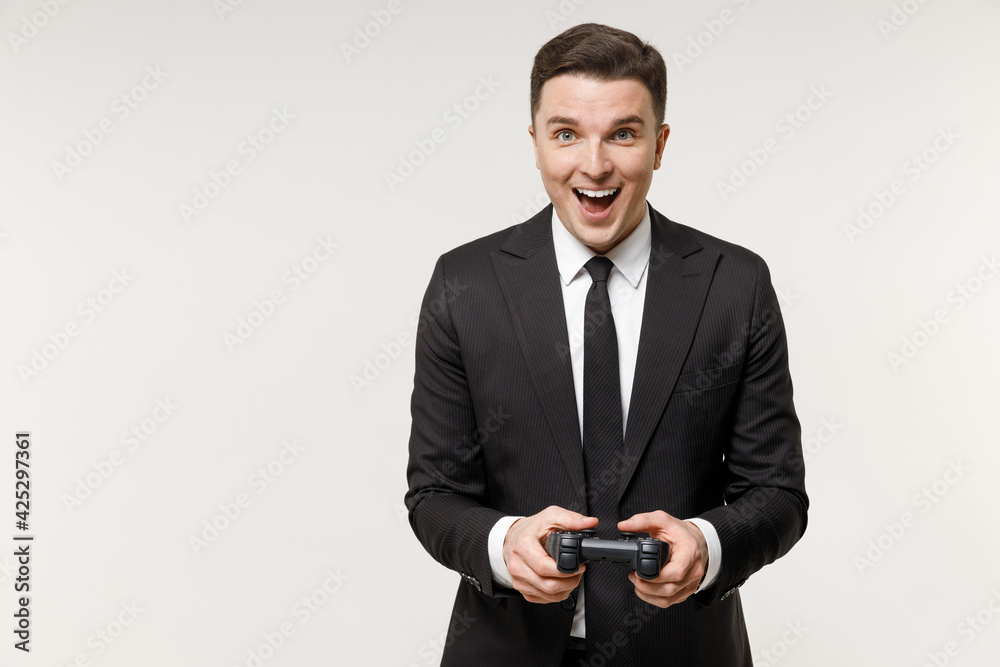 Young overjoyed rich employee business corporate lawyer man in classic formal black grey suit shirt tie work in office play pc game with joystick console isolated on white background studio portrait. Young overjoyed rich employee business corporate lawyer man in classic formal black grey suit shirt tie work in office play pc game with joystick console isolated on white background studio portrait.