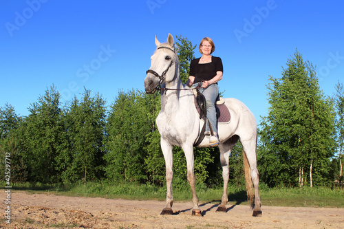 Elderly woman on a white horse enjoying a beautiful day-Concept of love between people and animals-Horse is a noble animal © Irina