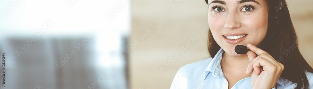 Brunette female customer service representative in a headset is consulting clients online. Call center and business people concept Brunette female customer service representative in a headset is consulting clients online. Call center and business people concept