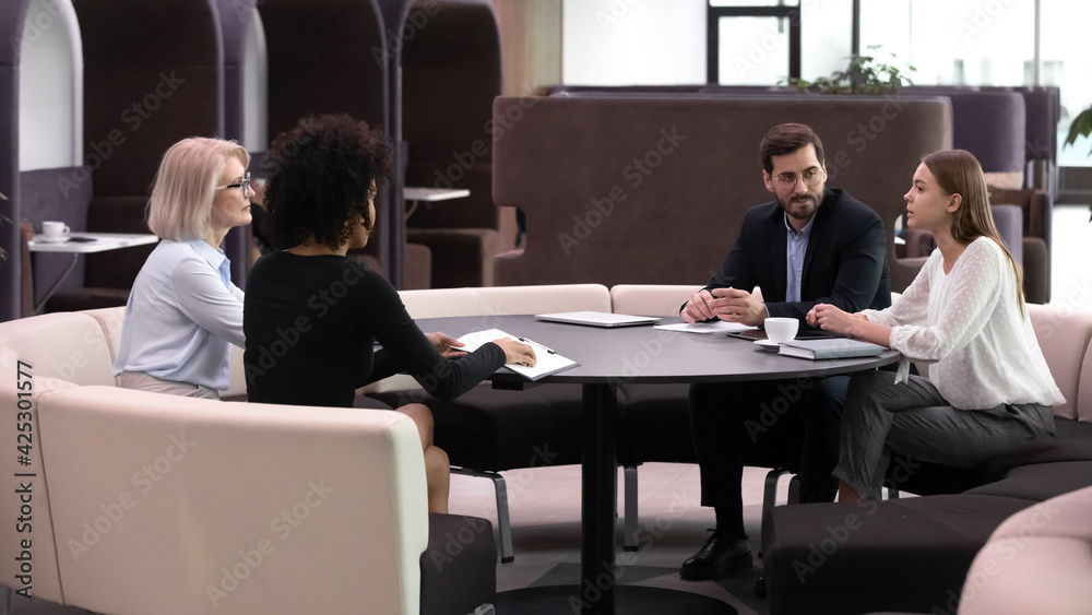 Diverse multiracial businesspeople sit in cafe have casual business meeting with clients customers. Multiethnic partners or employees talk discuss collaboration at briefing. Banking concept.