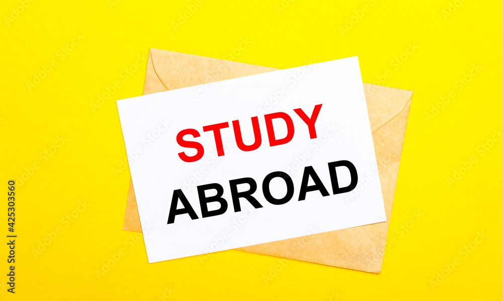On a yellow background, an envelope and a card with the text STUDY ABROAD. View from above On a yellow background, an envelope and a card with the text STUDY ABROAD. View from above