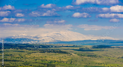 Beautiful winter landscape of Golan Heights: view of snow-capped Mount Hermon on a border with Syria and Lebanon - Israel's only ski resort, with green fields and clouds photo