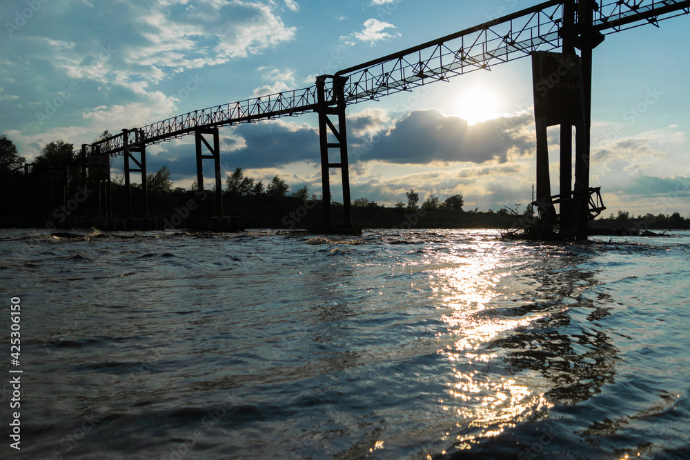 Fototapeta premium Beautiful waves of the river, on the far background, the old iron structure and a beautiful sunset.