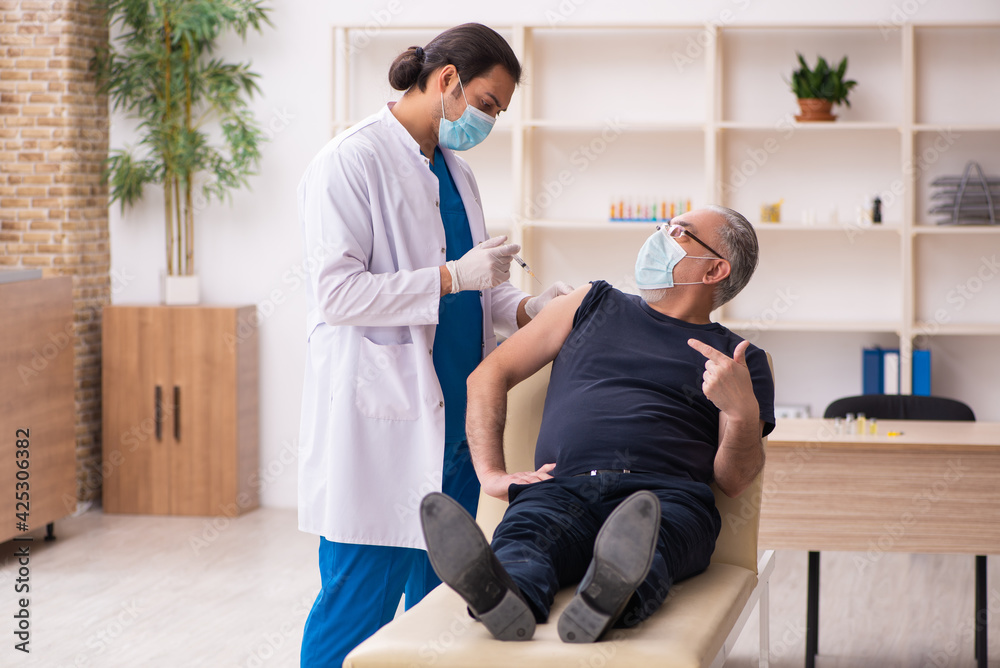 Fototapeta premium Old man visiting young doctor in covid-19 vaccination concept
