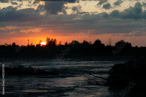 Evening sunset on the background of trees and antennas, in the foreground the river and a beautiful sky.