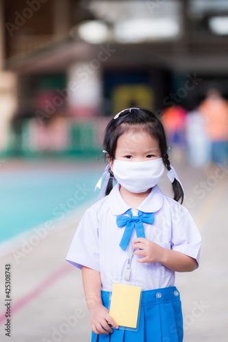 Kindergarten child wear white-blue school uniforms to school, kid wear white face mask to prevent the coronavirus (COVID-19) outbreak. New Normal. Cute girl aged 3-4 years old. Vertical image.