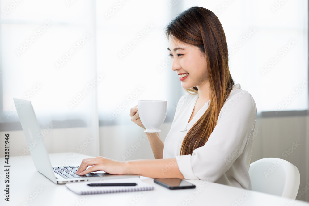 Young asian beautiful business woman working with laptop sitting at home drinking coffee. Smiling charming happy young female doing homework meeting conference with team at home. Young asian beautiful business woman working with laptop sitting at home drinking coffee. Smiling charming happy young female doing homework meeting conference with team at home.