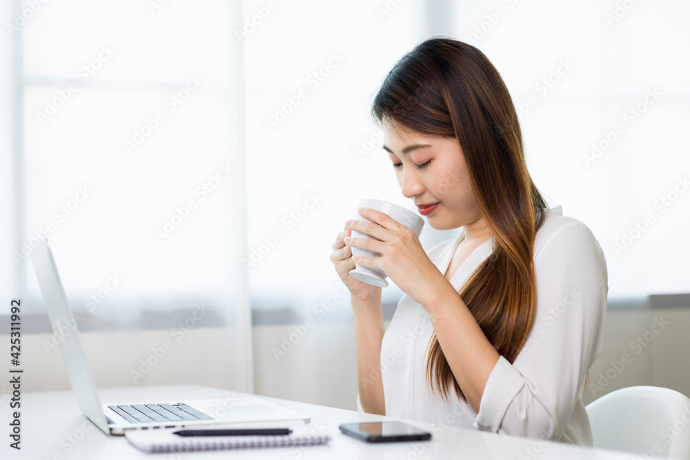Young asian beautiful business woman working with laptop sitting at home drinking coffee. Smiling charming happy young female doing homework meeting conference with team at home. Young asian beautiful business woman working with laptop sitting at home drinking coffee. Smiling charming happy young female doing homework meeting conference with team at home.