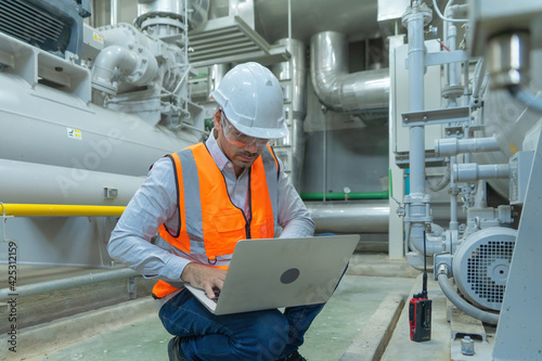 An engineer man or worker, people using a laptop computer, working in industry factory. Chiller tower or cooling tower in building. System work machine. Condenser Water Supply pipe lines. Ventilation.