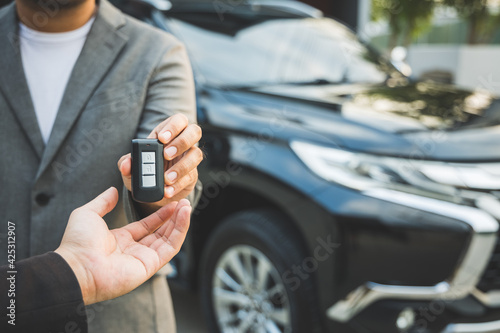 Close up businessman in suit his hands showing or giving car key for customer getting new car. Buy sell rent car concept.